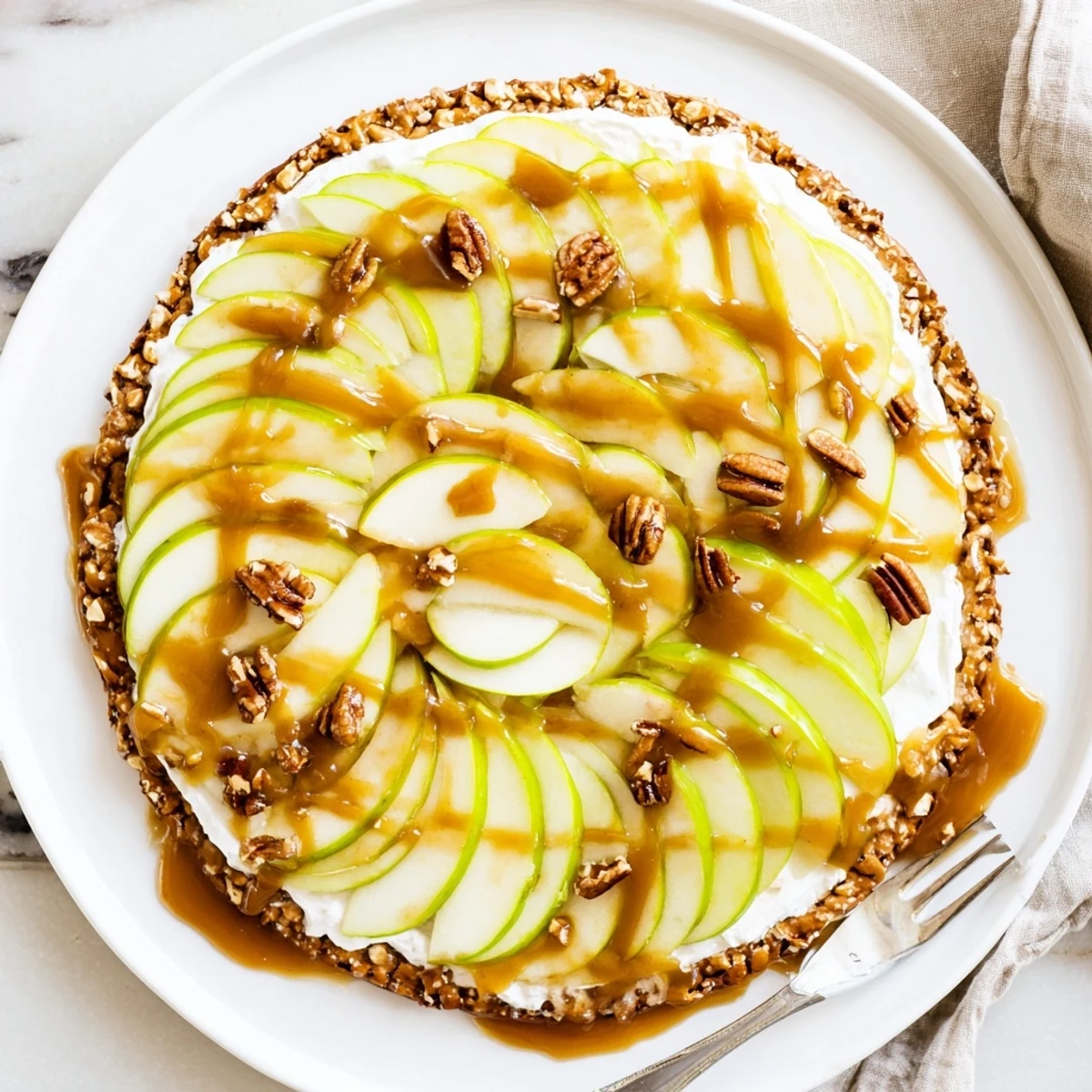 Sliced apples atop creamy caramel sauce on a sweet pretzel crust dessert pizza.