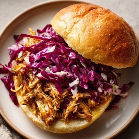 Tender slow cooker honey mustard chicken with tangy slaw, served on a toasted sandwich bun.