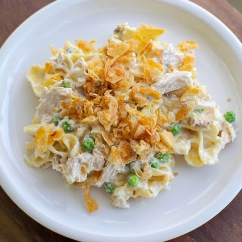 Warm, creamy Tuna Noodle Casserole with visible peas and cheese, perfect for a cozy dinner.