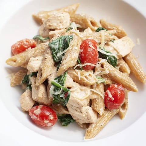 A close-up of steaming Greek Yogurt Chicken Pasta highlights golden chicken, vibrant green spinach, and a creamy, tangy sauce coating whole wheat penne.  