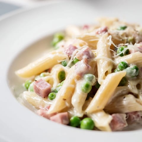 Bright green peas and browned ham fill a skillet of Spring Pea & Ham Pasta, steaming next to a glass of white wine.