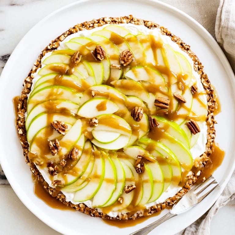 Sliced apples atop creamy caramel sauce on a sweet pretzel crust dessert pizza.
